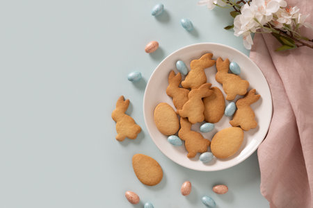 Homemade Easter bunnies shaped cookies and chocolate eggs on blue background. Top view. Space for text. Festive food and snacks. Greeting card.の写真素材