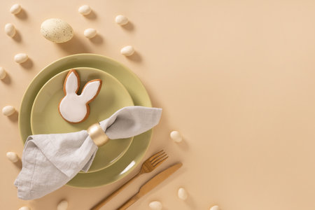 Easter table setting background with white plate, cookies , eggs and bunny on beige background. View...