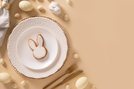 Easter table setting background with white plate, cookies , eggs and bunny on beige background. View...