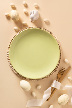 Easter table setting with white plate, decorative eggs and bunny on beige background. View from...
