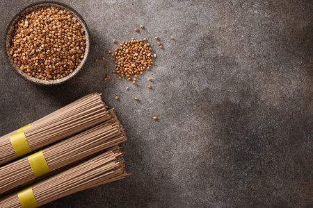 Uncooked buckwheat noodles, soba and grain in bowl on dark gray background. View from above. Space for text. Healthy vegan diet. Alternative gluten free pasta.の写真素材