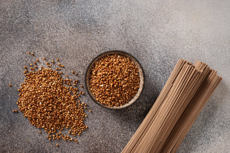 Uncooked buckwheat noodles, soba and grain in bowl on dark gray background. View from above. Space for text. Healthy vegan diet. Alternative gluten free pasta.の写真素材