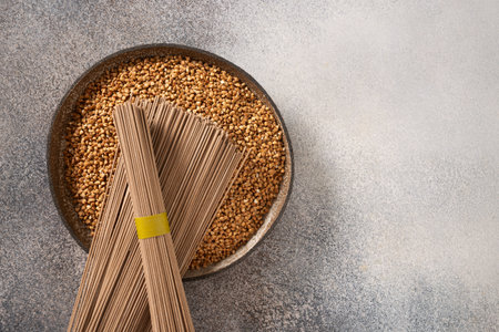 Uncooked buckwheat noodles, soba and grain in bowl on gray background. View from above. Space for text. Healthy vegan diet. Alternative gluten free pasta.の写真素材