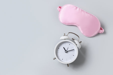 Pink sleeping mask and watch, alarm on gray background. Concept of sleep, health care, daily routine and circadian rhythms. Copy space.の写真素材