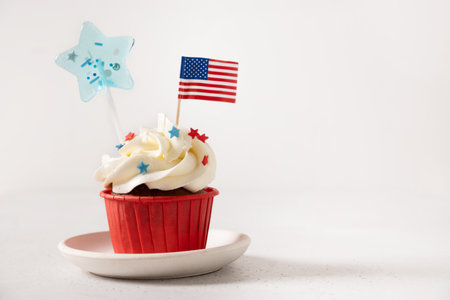 Traditional American sweet cupcake with festive stars and USA flag on white background. Dessert for...