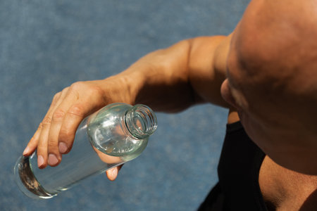 Athletes man drinking water on outdoor sports ground. Concept water balance for hot season for...