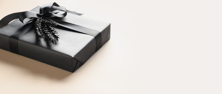 Black gift box with bow on beige background. Banner. Close up. Copy space. Present for Father Day,...
