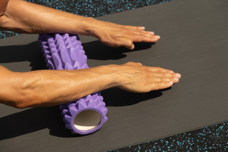 Athlete mans hands exercising and stretching arms on foam roller on sports ground. Outdoor activity. Close up.の写真素材
