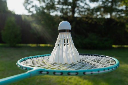White badminton shuttlecock and badminton rackets on green grass in sunny shadow. Summer. Leisure...