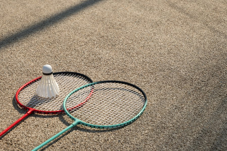 White badminton shuttlecock and two badminton rackets in sunny shadow on beige floor sport badminton...