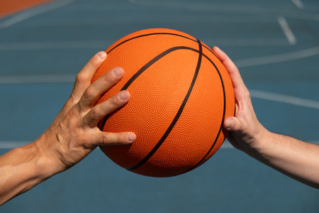 Hands of two basketball players holding orange ball on sports court. Sports goals competition game,...