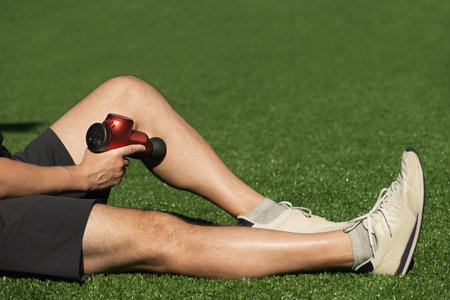 Man massaging body and legs with massage percussion device after workout. Applying therapeutic percussion massager gun.の写真素材