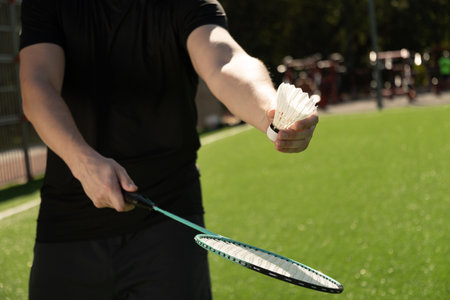 Mans hands with badminton racket and shuttlecock on sport court in sunny day. Outdoors. Close up.の写真素材