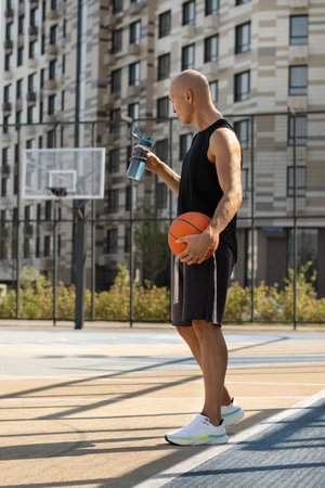 Basketball player taking break from playing match and drinking water on sports court outside. Game interval. Summer outdoors training.の写真素材