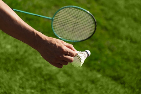 White badminton shuttlecock and badminton racket in man hands. Summer sports game. Outdoor activity. Close up. Copy space.の写真素材