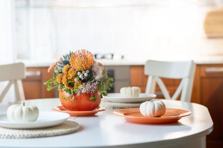Thanksgiving day table setting decoration with creative bouquet centerpieces orange flowers in pumpkin as vase in modern home kitchen interior. Close up.の写真素材