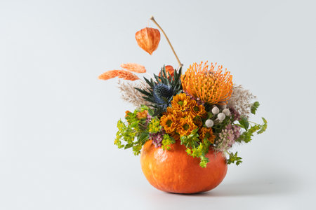 Autumn banner with creative bouquet of orange and yellow flowers in pumpkin as vase on gray background. Thanksgiving Day. DIY. Copy space. Floral composition.の写真素材