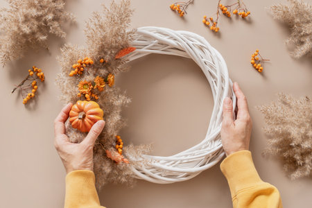 Woman making wreath with orange flowers and dry natural materials over beige background. Top view. Workshop for handmade Thanksgiving day decoration.の写真素材