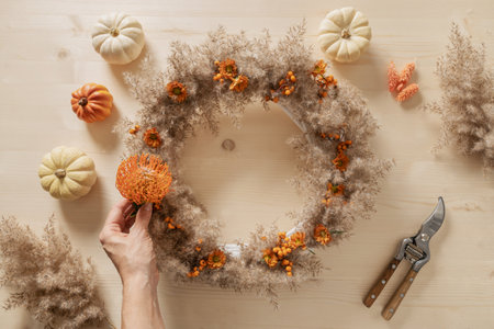 Woman making wreath with orange flowers and dry natural materials on wooden desk. Top view. Workshop for handmade Thanksgiving day decoration.の写真素材