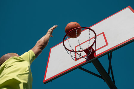 Basketball player or sporty man tries to throw ball into basketball hoop on sports court at...