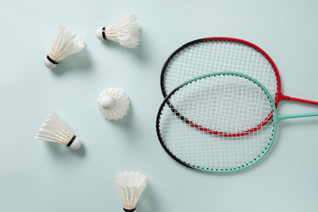 White feather badminton shuttlecocks and two badminton rackets on light blue background. View from above. Concept racket sport. Leisure games.の写真素材