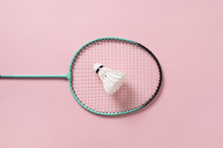 White feather badminton shuttlecock and badminton racket on light pink background. View from above. Concept racket sport. Leisure games.の写真素材