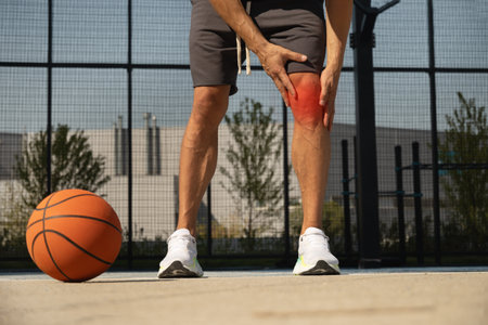 Basketball knee injury or pain. Basketball player check legs after workout of sport stadium. Professional athlete or sportsman with accident. Man holding leg after training or sport workout.の写真素材