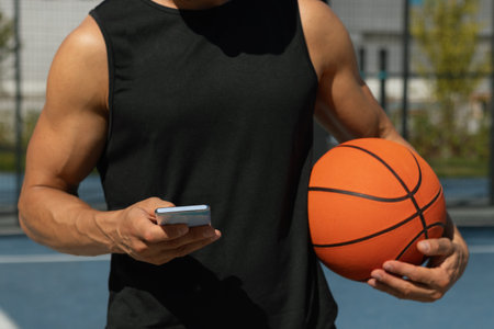 Basketball player or sports caucasian man using smartphone after outdoor training. Outdoors game. Relax, game interval.の写真素材