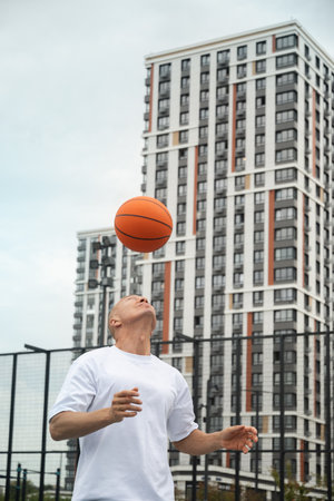 Basketball player with orange ball on sports court at courtyard. Street and urban style. Fun exercise. Game moment.の写真素材