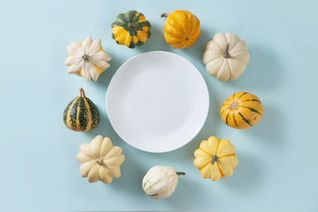 Autumn colorful pumpkins around empty white plate on blue background for Thanksgiving day. Copy space. View from above. Harvest day conceptの写真素材