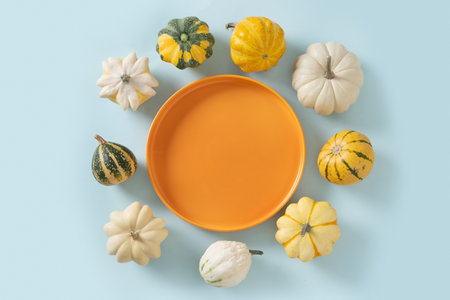 Autumn colorful pumpkins around orange plate on blue background for Thanksgiving day or Halloween. Copy space. View from above. Harvest day conceptの写真素材