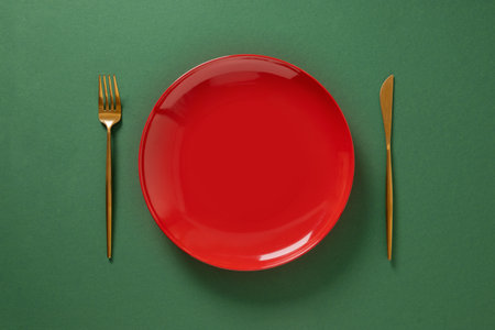 Christmas table setting with red empty plate on green background. Xmas festive dinner celebration, winter holiday. Top view. Copy space.の写真素材