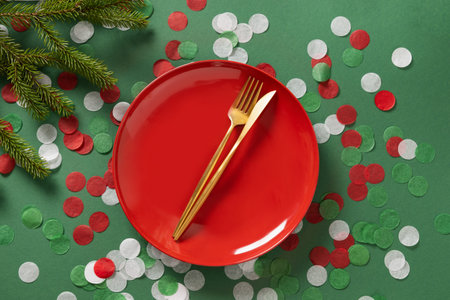 Christmas table setting with red empty plate and golden cutlery on green background. Xmas festive dinner celebration, winter holiday. Top view. Copy space.の写真素材