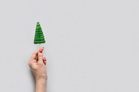 Christmas tree shaped green lollipop in woman hand. Xmas creative minimal greeting card. View from above. Copy spaceの写真素材