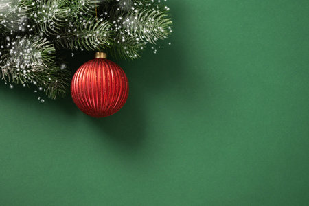 Christmas red bauble on fir snowy branches on green background. Xmas greeting card. New Year banner. Copy space. View from above.の写真素材