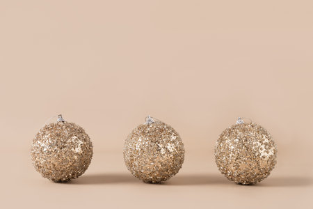 Christmas three golden shiny baubles in row on beige background. Xmas greeting card. New Year concept. Trendy color of New 2025 Year. Copy space.の写真素材