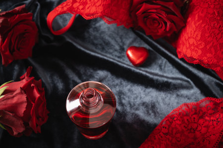 Romantic dating. Valentines day, lace womens red underwear, lingerie, massage oil and red roses on dark bedclothes. Body massage. Copy space. Close up.の写真素材