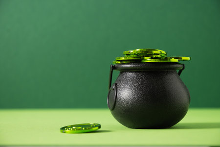 St. Patricks day black pot, treasure of leprechaun, pot full of green coins on festive green background. Close up. Greeting card.の写真素材