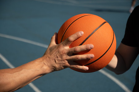 Hands of two basketball players holding orange ball on sports court. Sports goals competition game,...