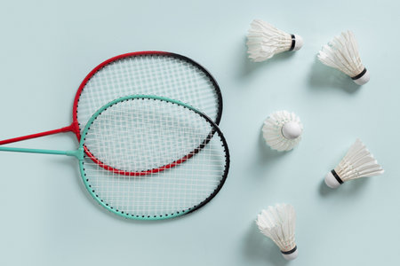 White feather badminton shuttlecocks and two badminton rackets on light blue background. View from...