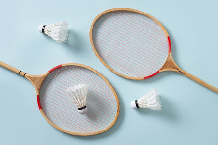 Two wooden badminton rackets and white feather badminton shuttlecocks on green background. View from...