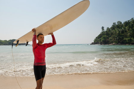 Handsome man surfer carrying surf and comes back from surfing. Outdoors. Sri Lanka. Tropical...
