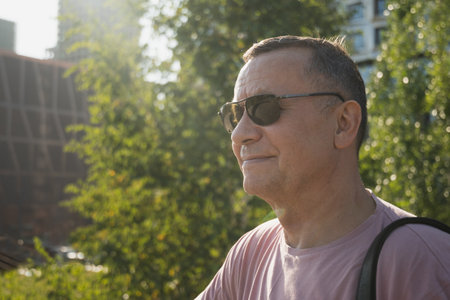 Portrait of smiling adult man wearing sunglasses and pink t-shirt at summer park. Outdoors. Close...