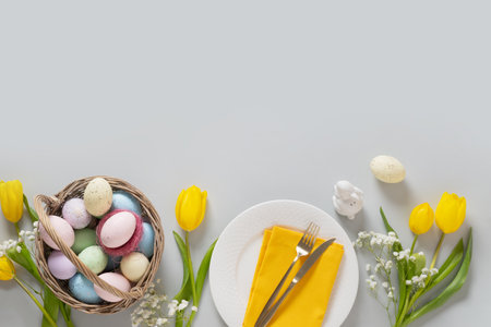 Easter frame with pastel colorful eggs, table setting decorated yellow tulip flowers on gray...