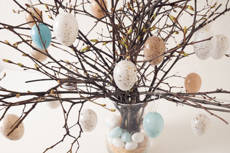 Easter tree decorated colorful pastel white and beige eggs. Birch branches with hang eggs in vase on...