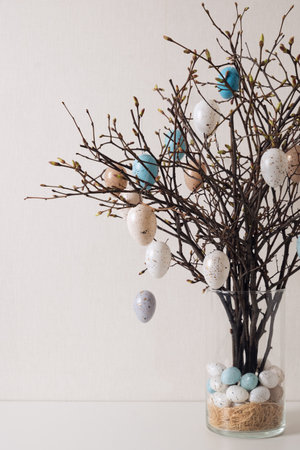 Easter tree decorated white and beige eggs in glass vase on white table. Vertical format. Happy...