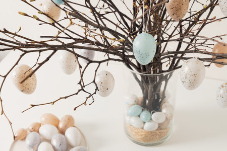 Easter tree decorated colorful pastel white and beige eggs. Birch branches with hang eggs in vase on...