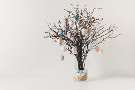 Easter tree decorated colorful pastel white and beige eggs. Birch branches with hang eggs in vase on...