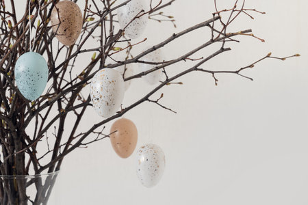 Easter tree decorated colorful pastel white and beige eggs. Birch branches with hang eggs in vase on...