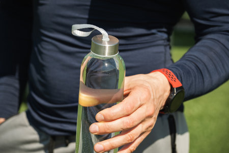 Athlete or sporty man holding water bottle on outdoor sports ground. Concept water balance for hot...